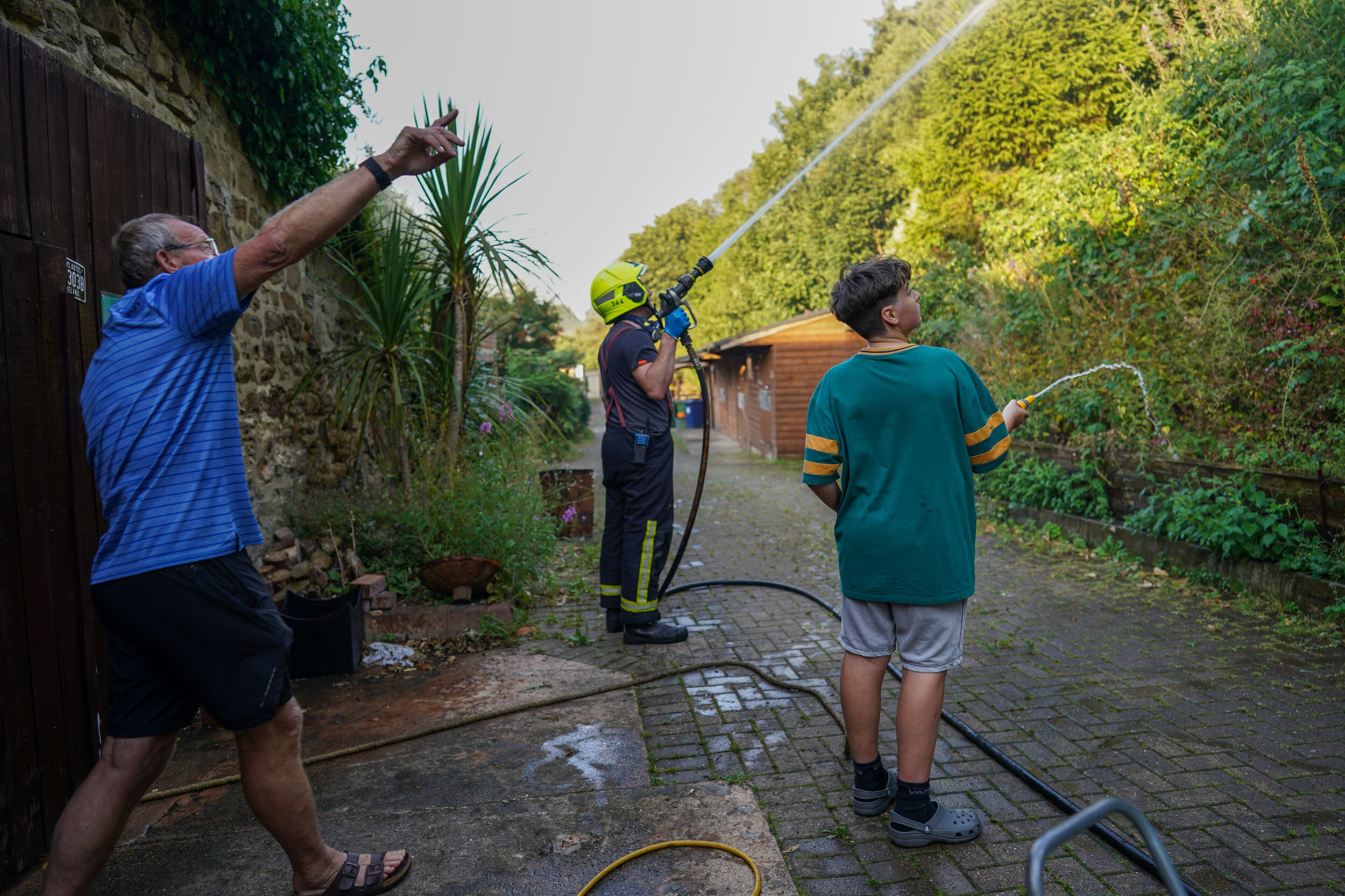 Local residents use garden hoses to assist fire crews tackle a crop fire that swept over farmland and threatened local homes on August 11